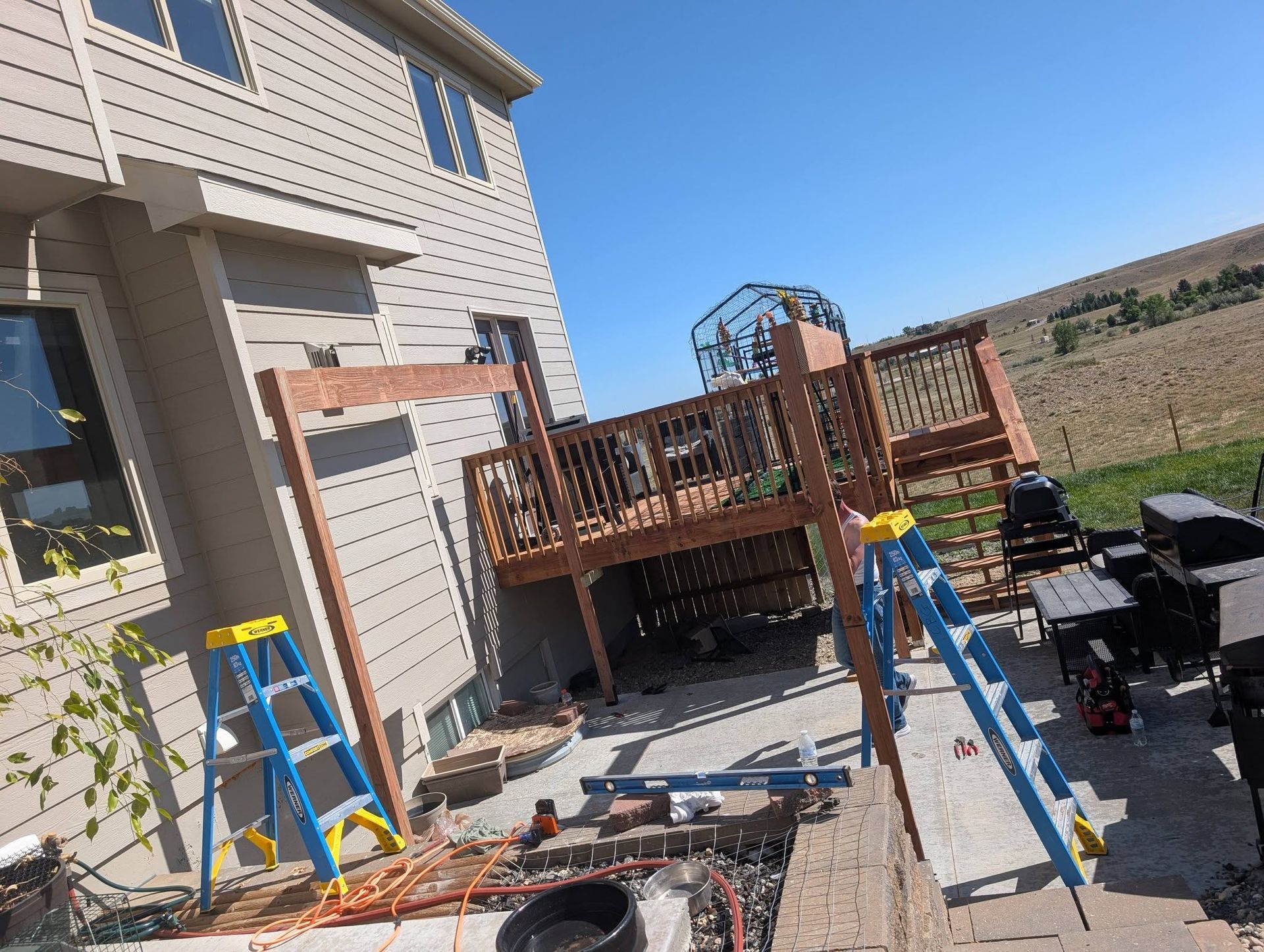 Backyard deck construction beside a house, with ladders, tools, and partially built railing.
