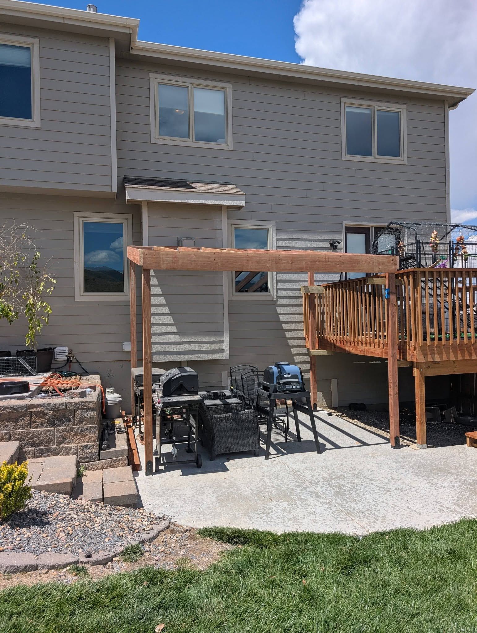 Backyard patio with wooden deck, pergola, stone pavers, and two-story house exterior