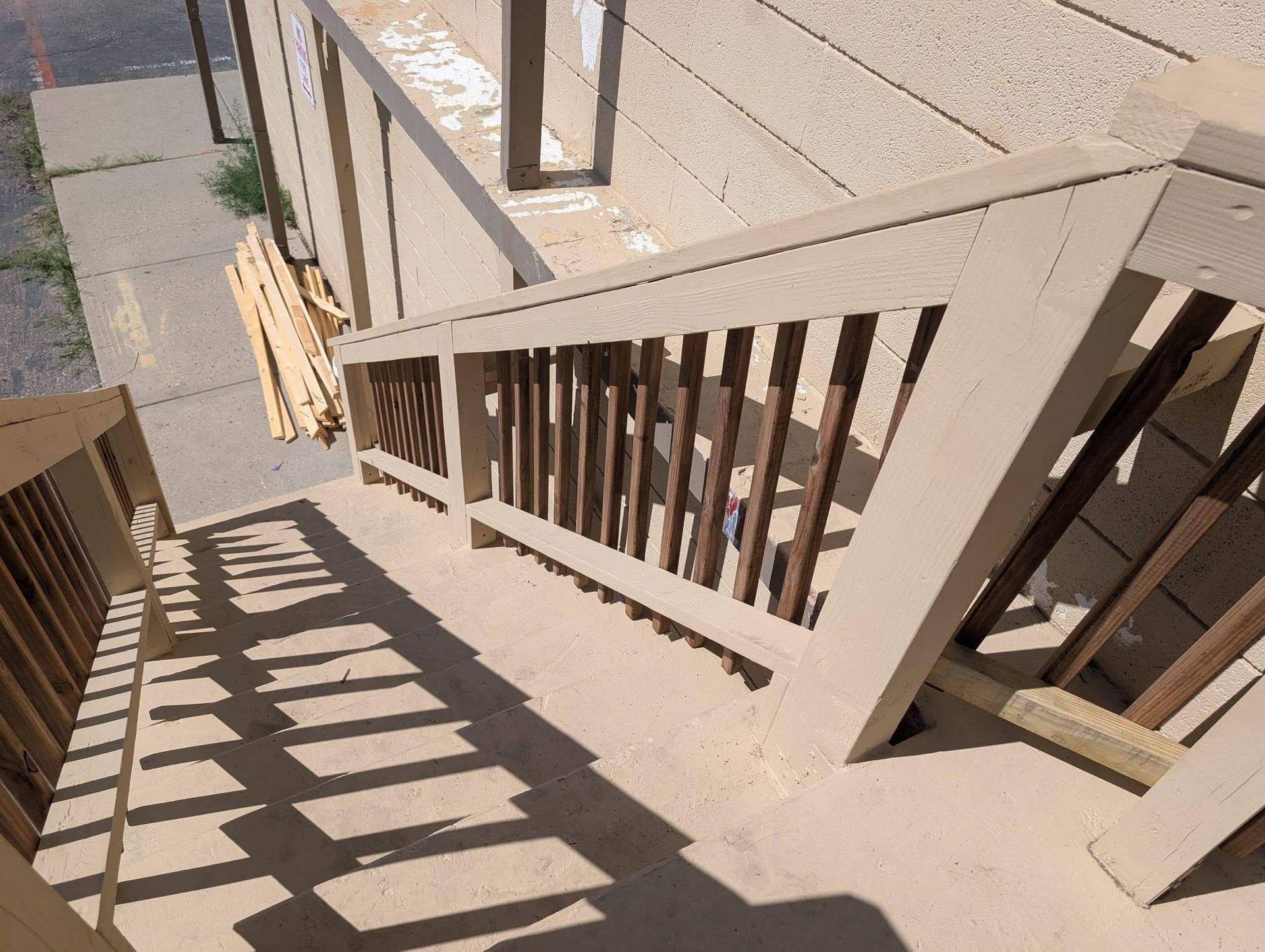 Sunlit outdoor staircase with beige railings casting striped shadows on concrete steps.