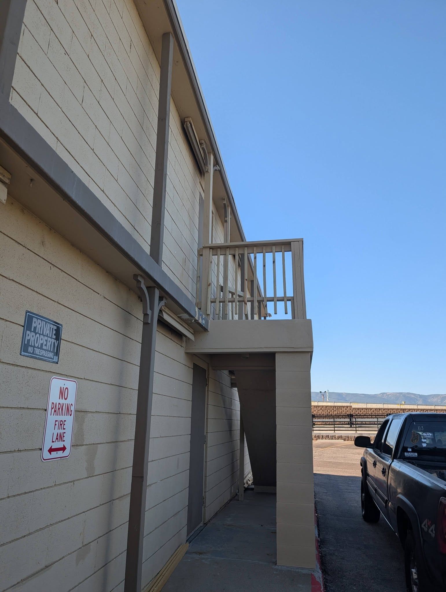Exterior of beige townhouse with balcony and parked pickup truck in a dry residential area