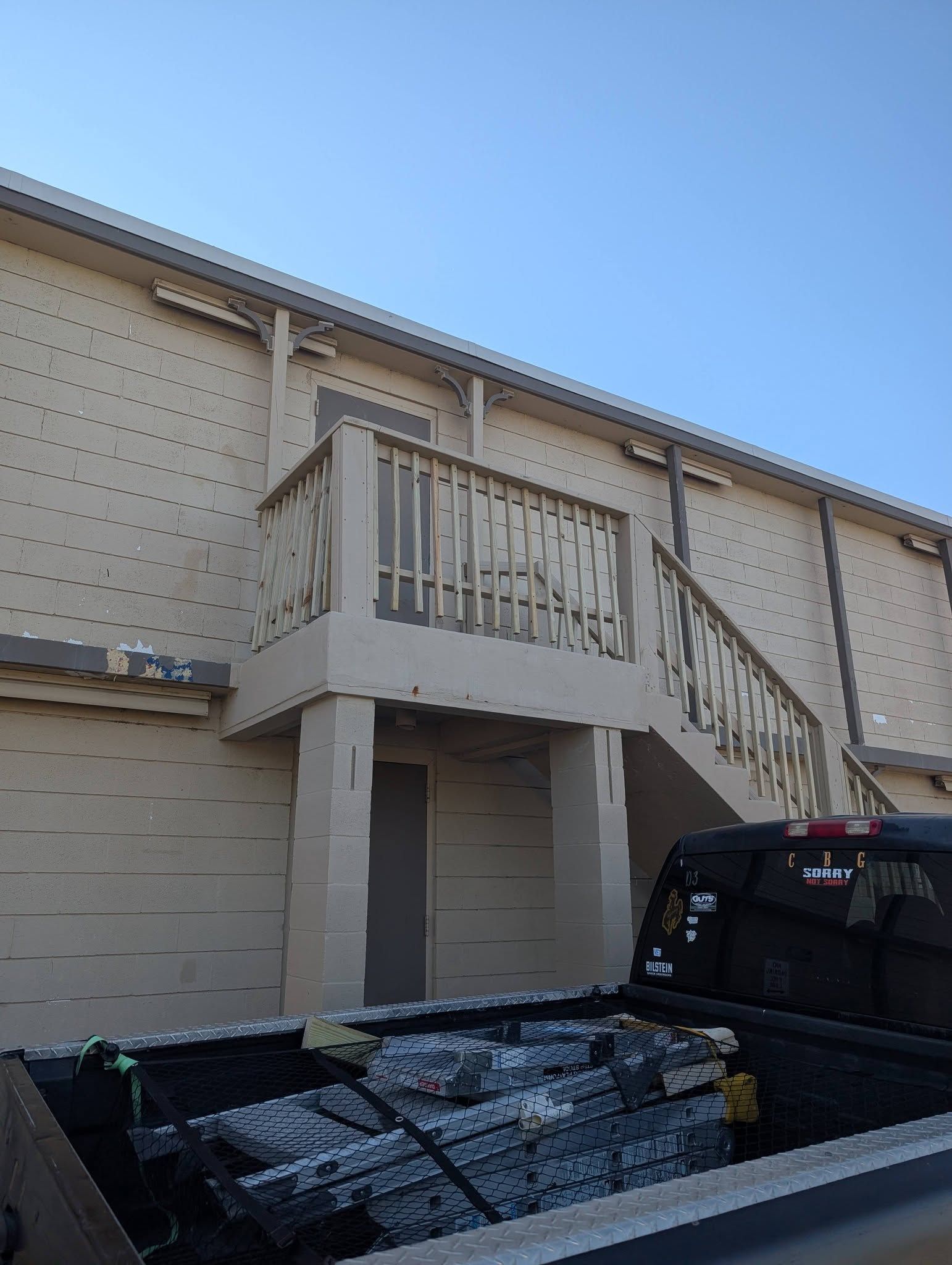 Exterior stairway and balcony on a beige apartment building, with a black truck parked below.