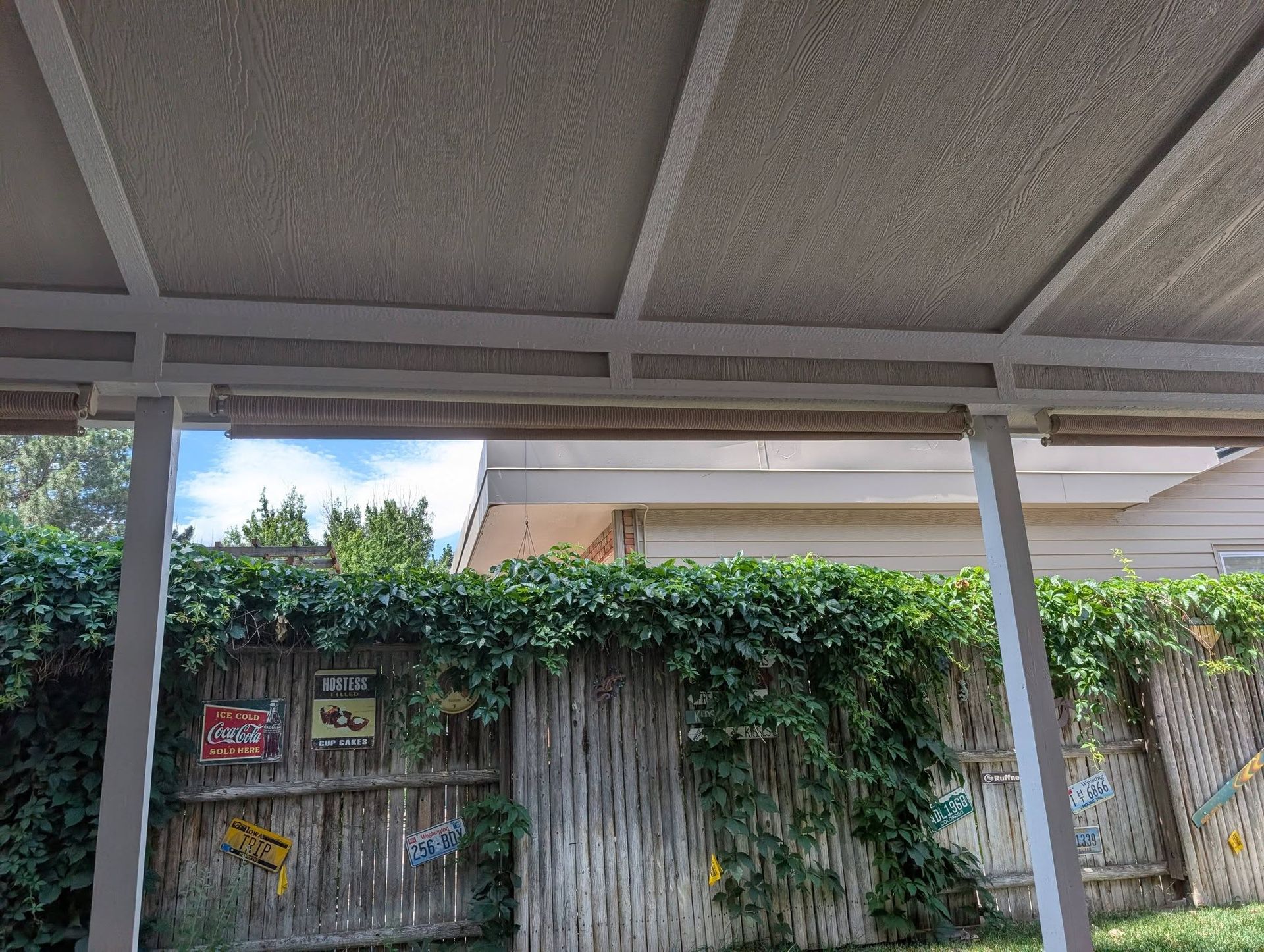 Concrete patio roof framing over an ivy-covered wooden fence with warning signs.
