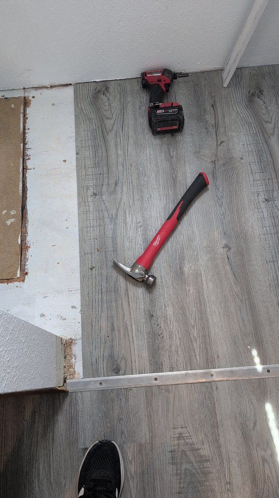 Red hammer and cordless drill on gray wood floor near a wall and stair edge.