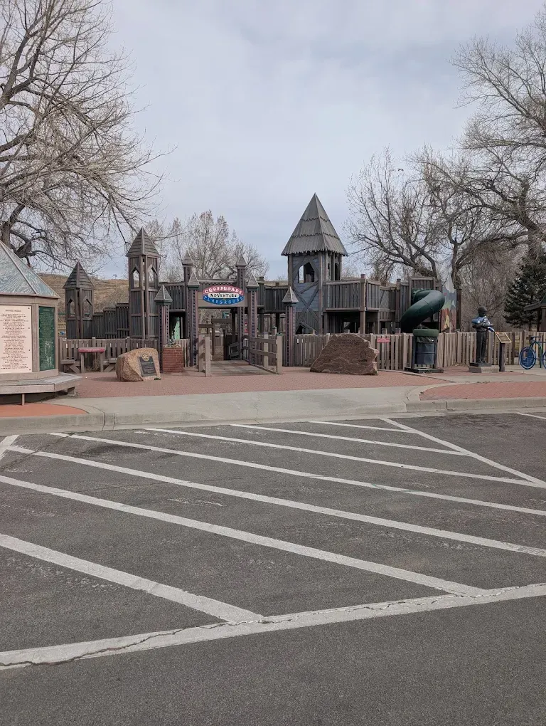 Empty playground with play structures, leafless trees, and a parking lot in the foreground.