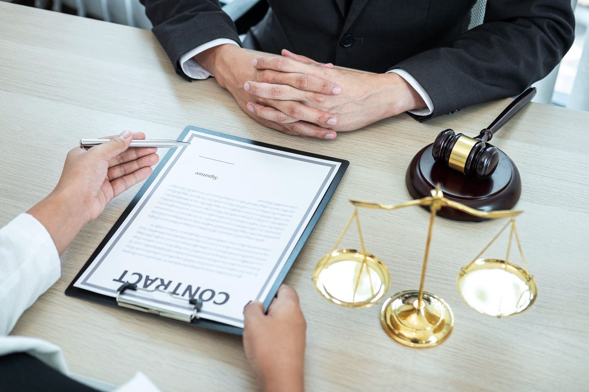 Lawyer across desk reviewing contract beside gold scales and gavel