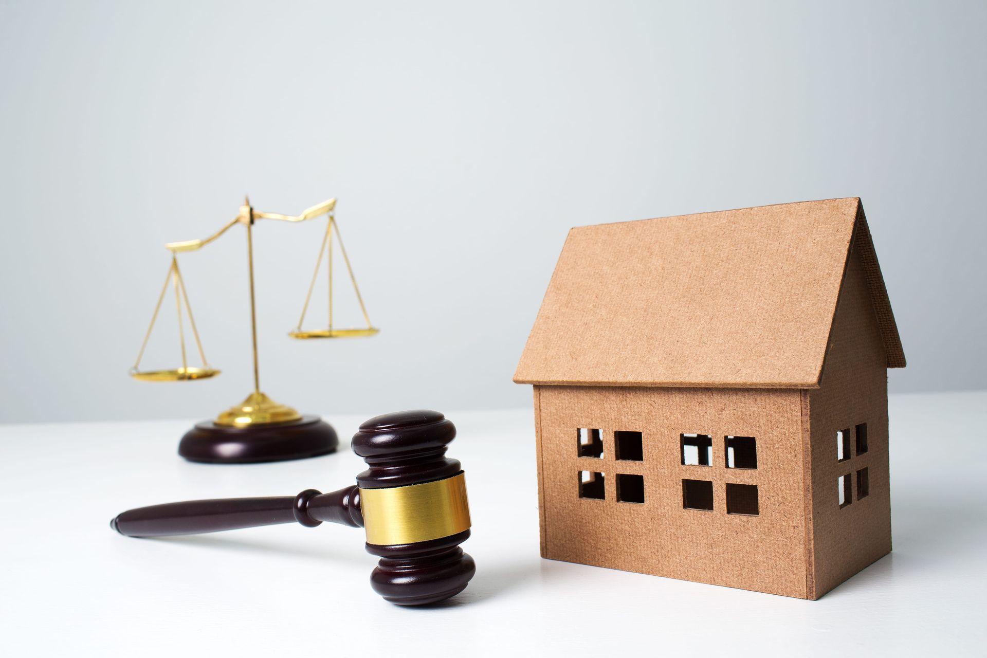 Judge’s gavel, golden scales, and a small house model on a white background