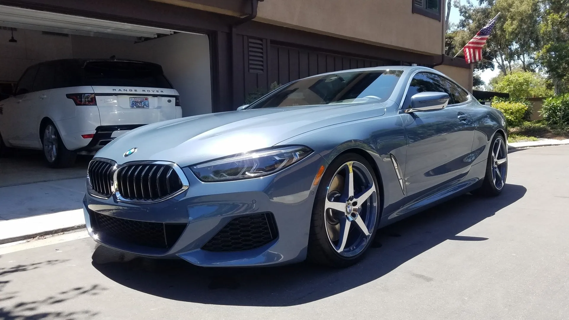 Blue BMW coupe parked in front of a garage, with a white Range Rover inside.