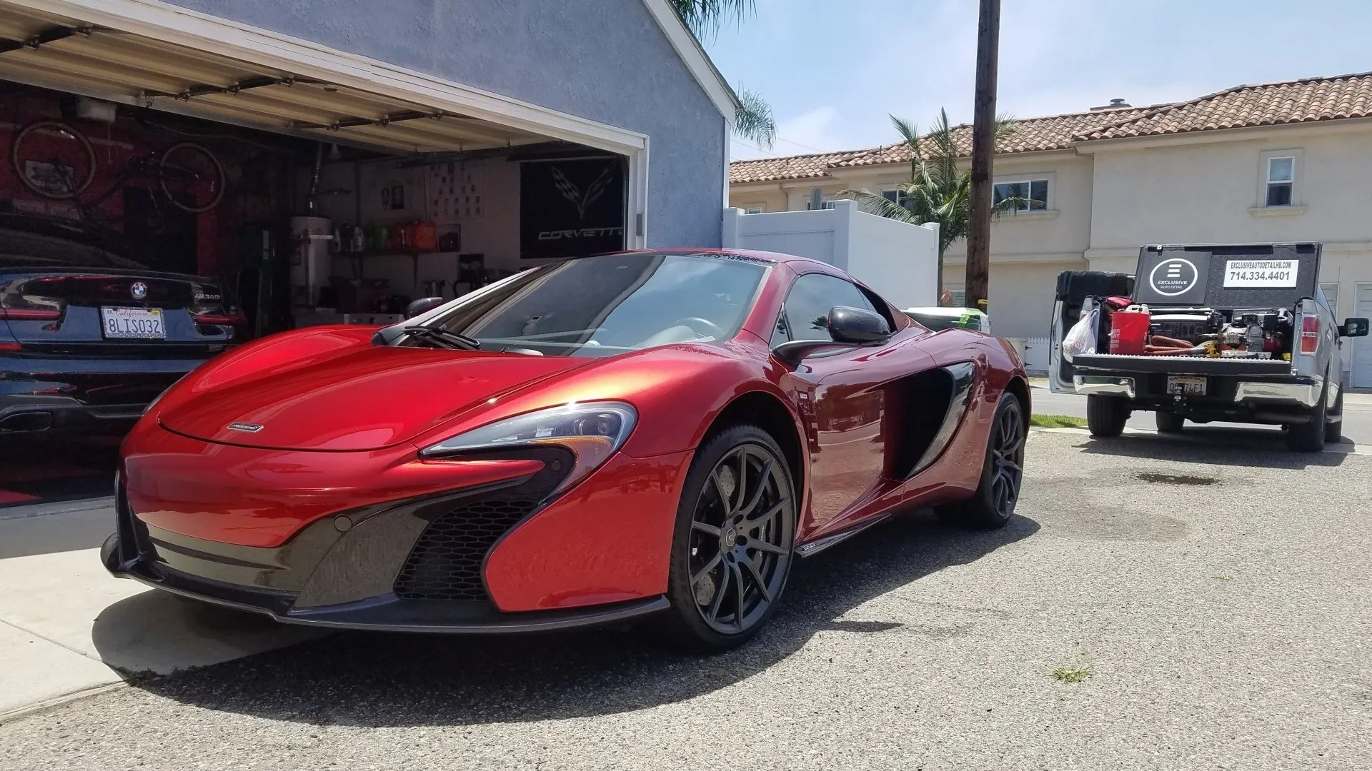Red McLaren sports car parked in a driveway in front of a garage, with a white truck nearby.