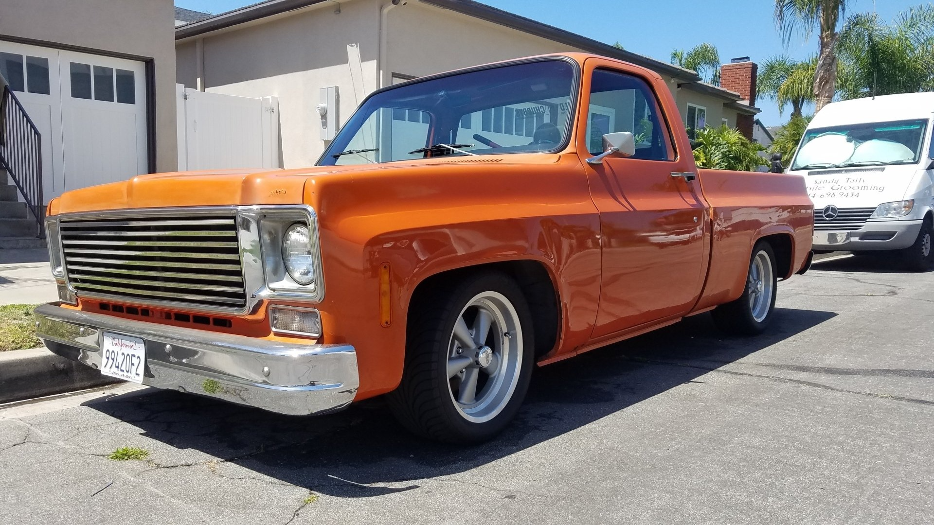 Orange classic pickup truck parked on a residential street. Silver grill and rims. Sunny day.