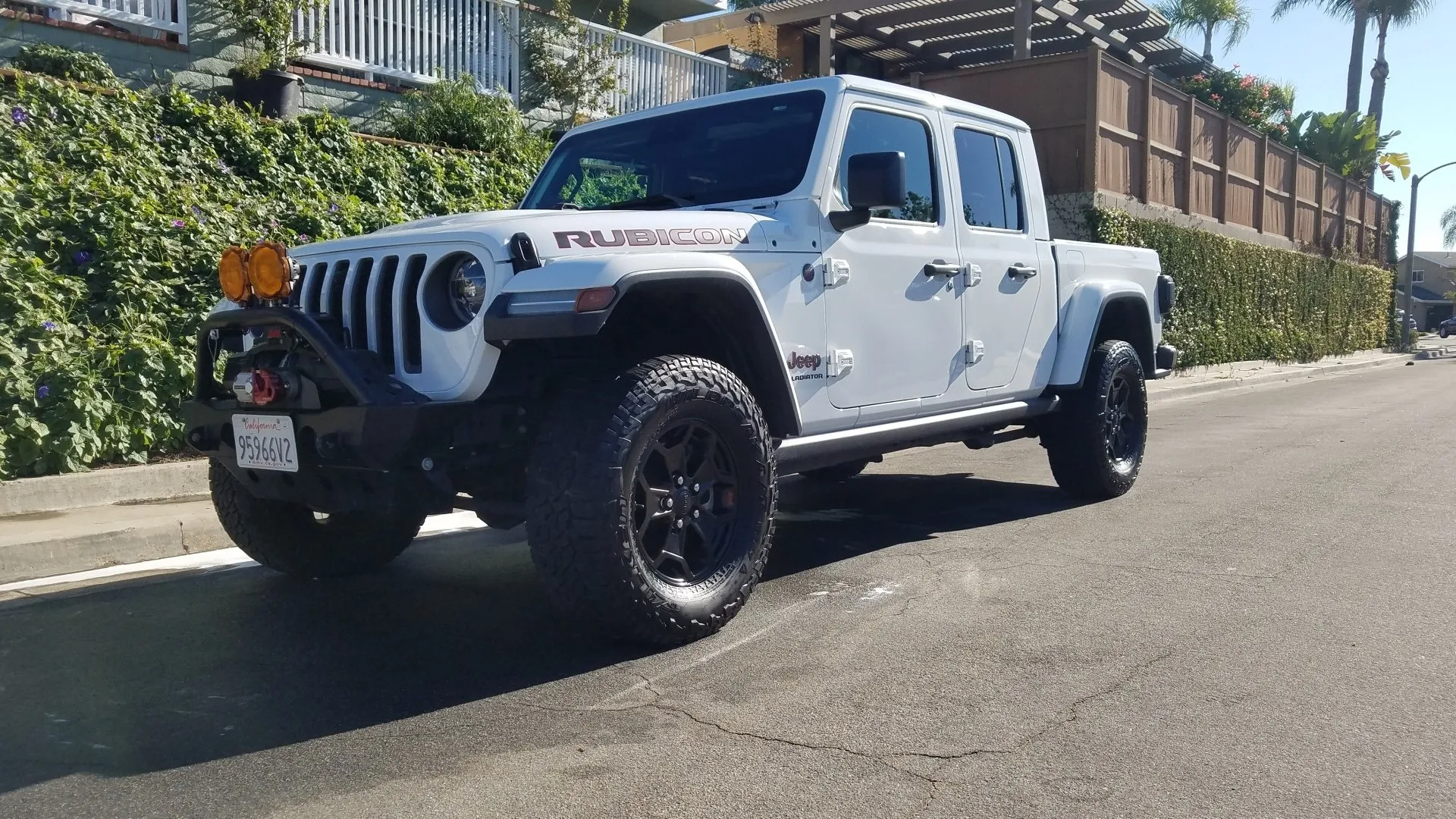 White Jeep Gladiator pickup truck parked on asphalt road. Black wheels, off-road features. California license plate.