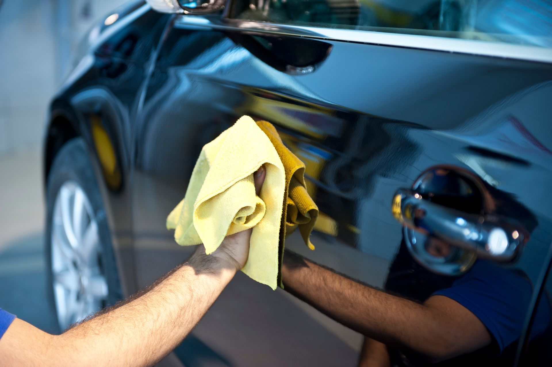 Person polishing a shiny black car with a yellow cloth.