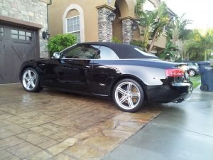 Black Audi convertible parked on a paved driveway in front of a house.