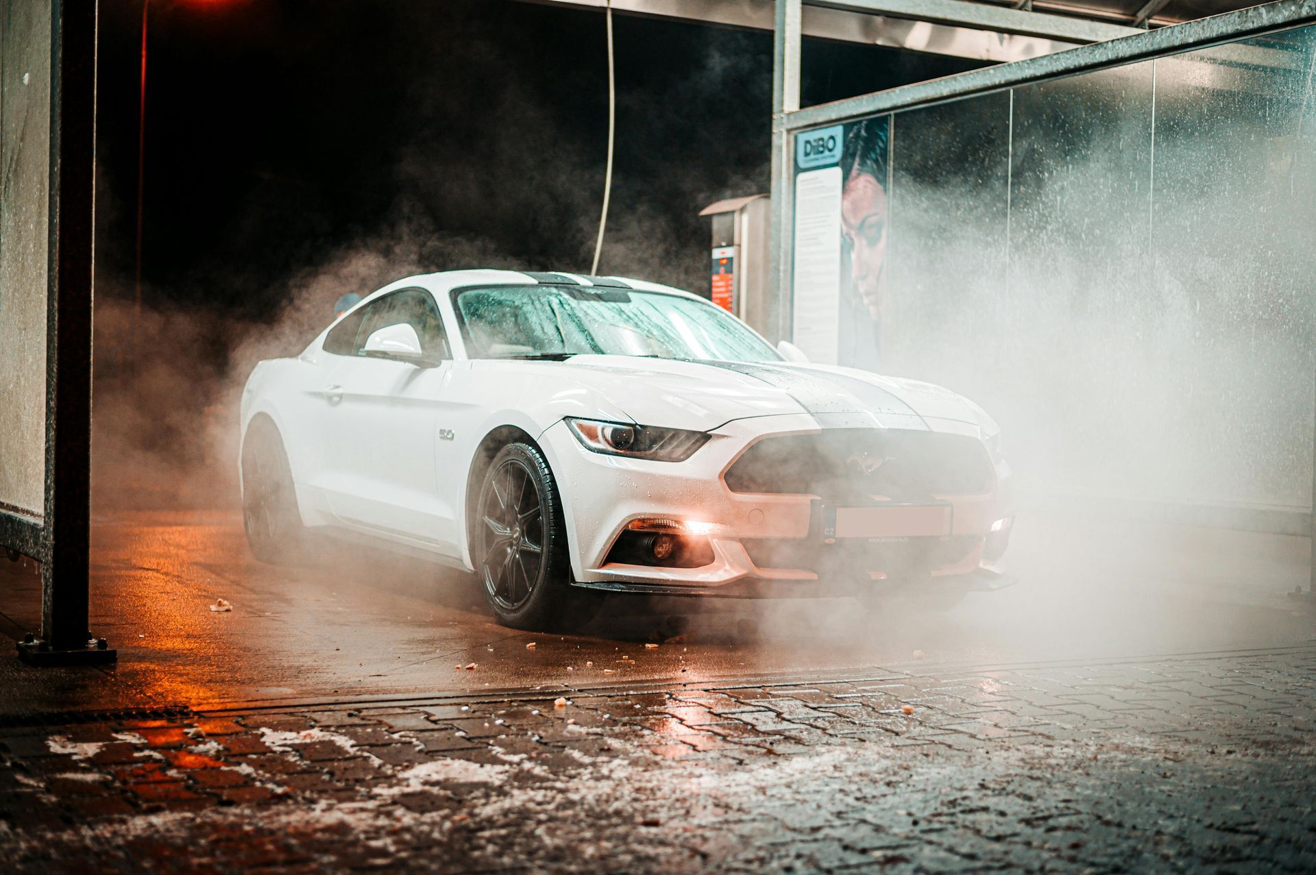 White Ford Mustang being washed at a car wash, water and mist surrounding.