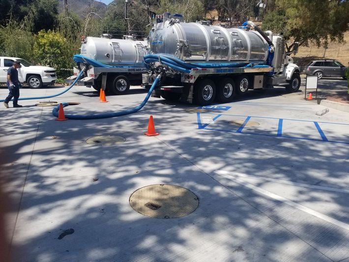 A man in orange overalls is pumping water from a truck.