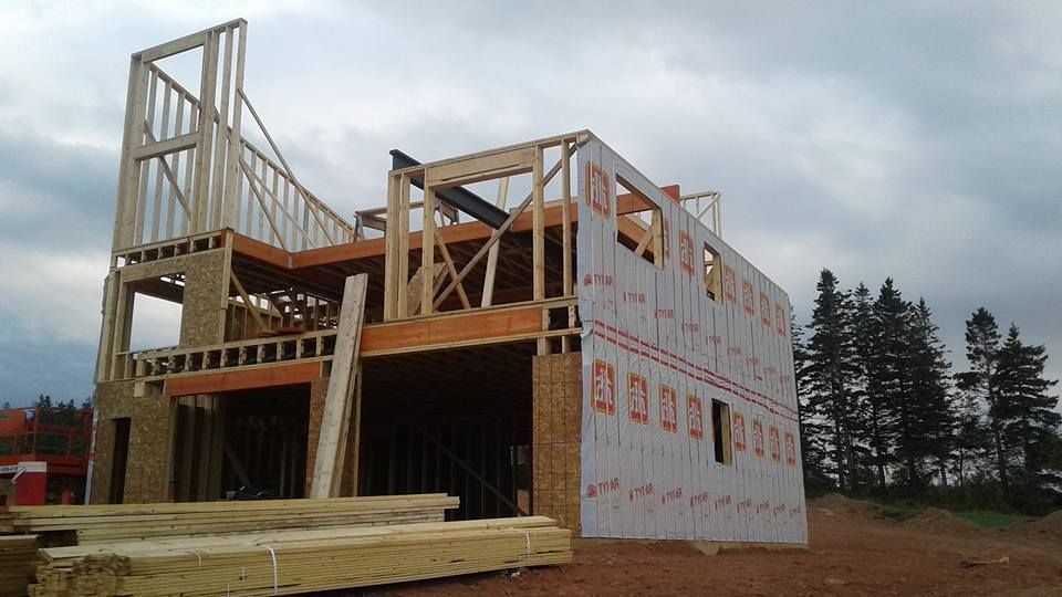A large wooden house is being built in a field with trees in the background.