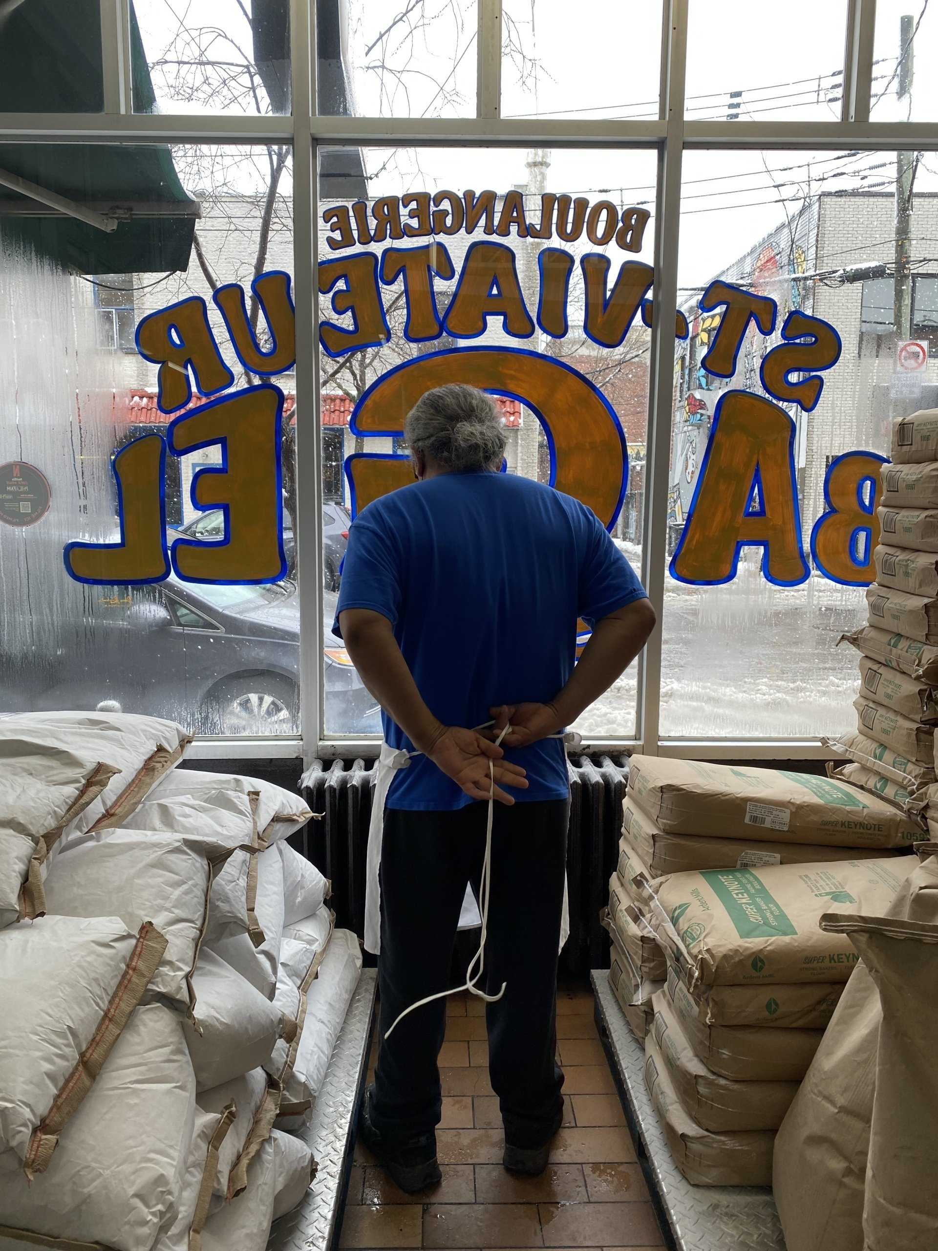A man in a blue shirt stands in front of a window that says ' sustain ' on it
