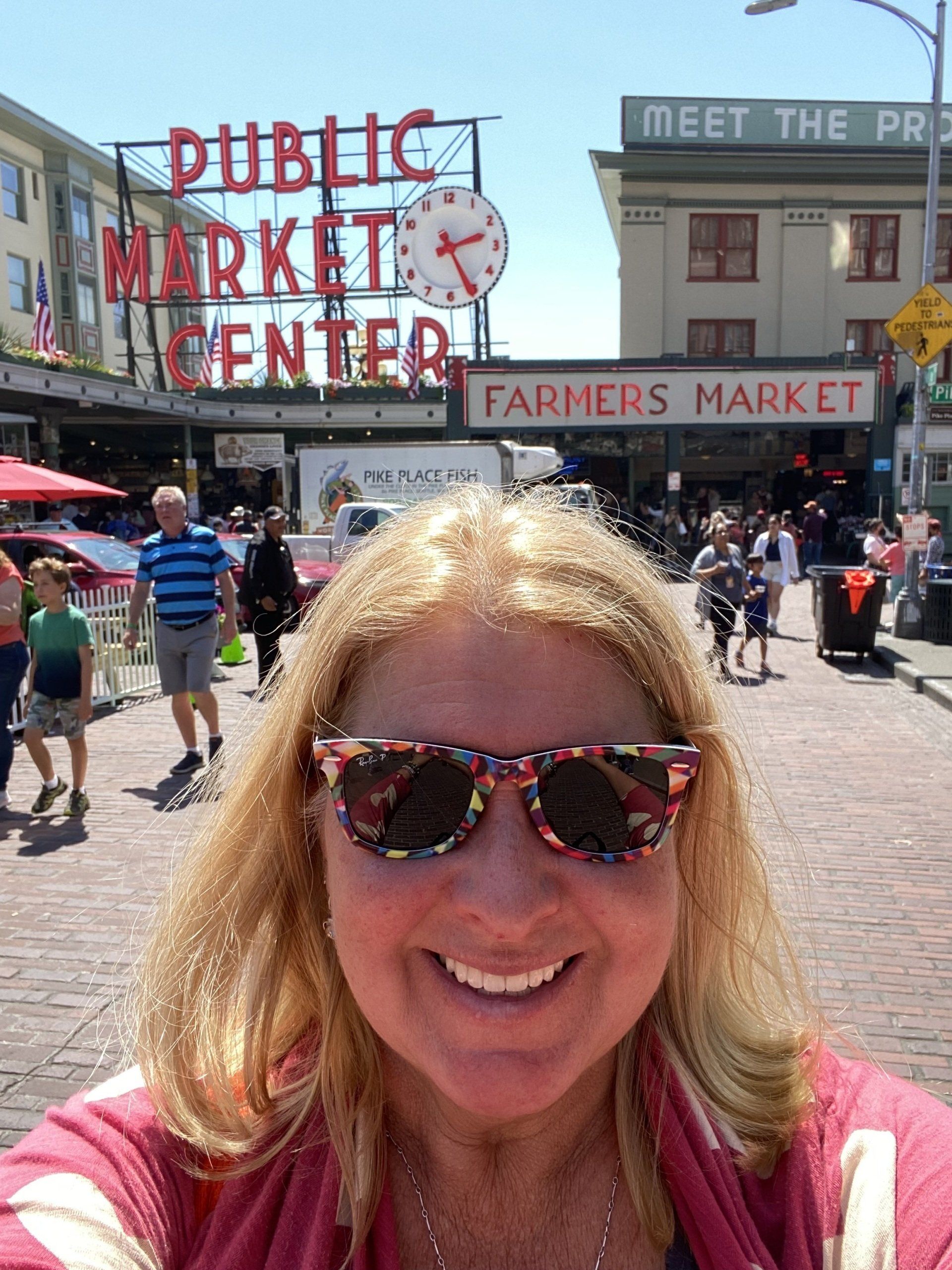 A woman wearing sunglasses is taking a selfie in front of the public market center