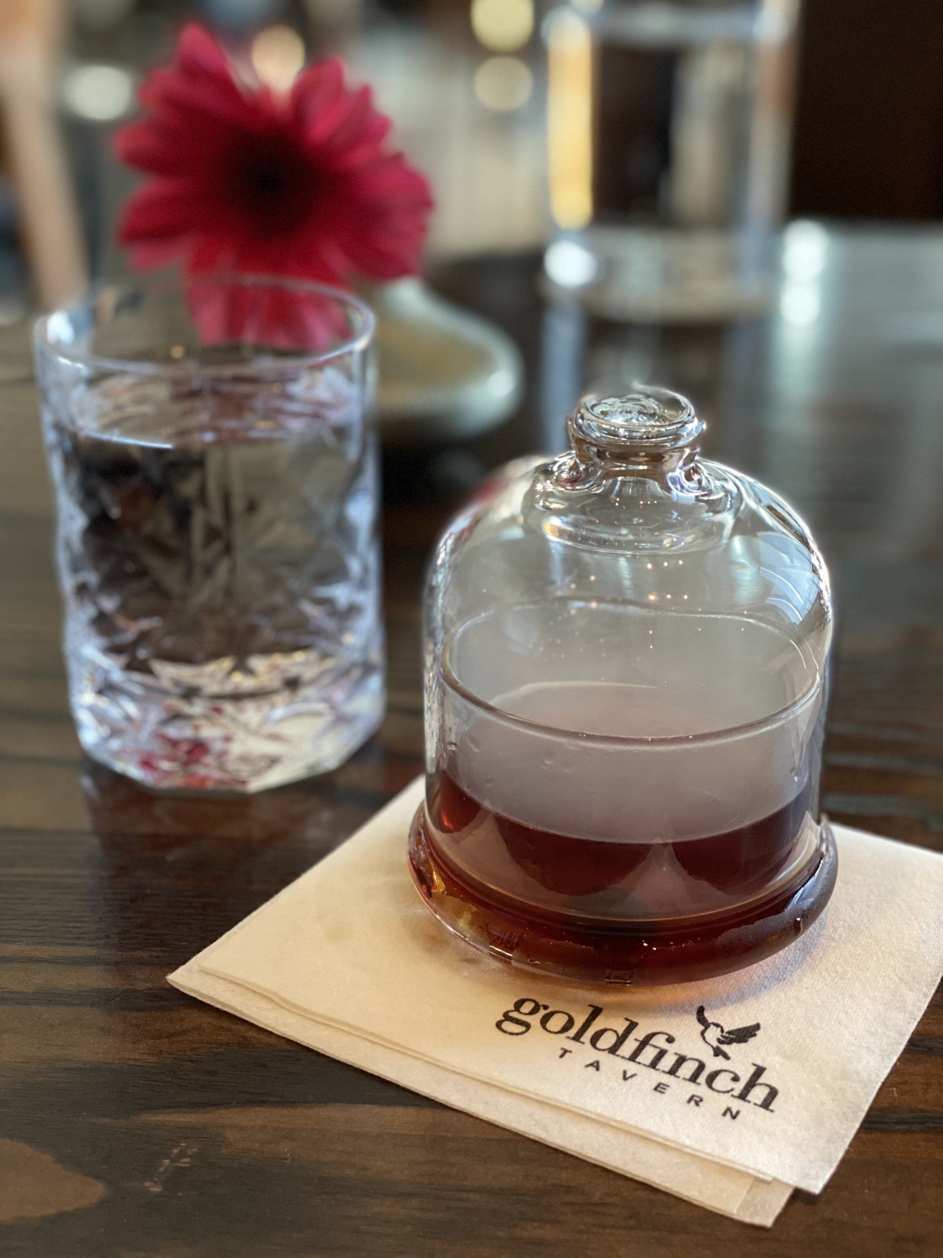 A glass of water and a glass of syrup on a napkin with goldfinch written on it