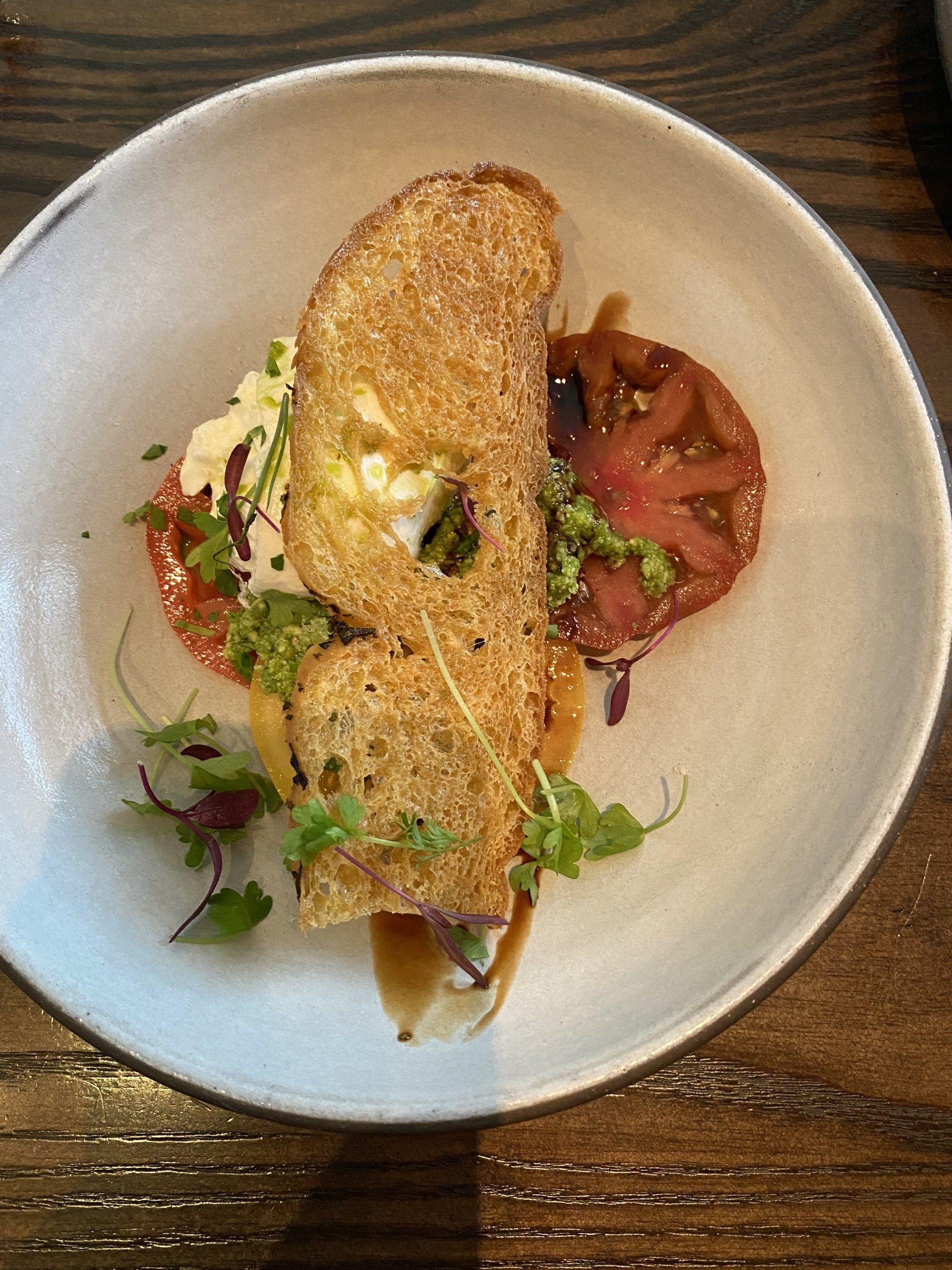 A white plate topped with a piece of bread and tomatoes on a wooden table.