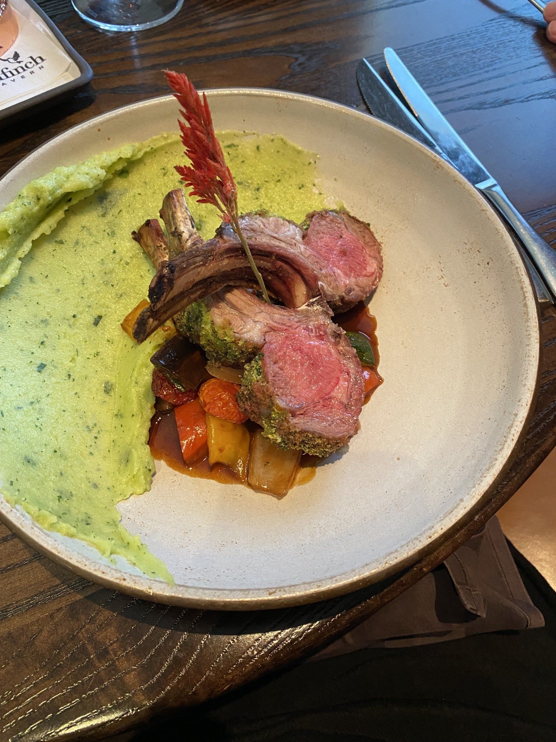 A white plate topped with meat and vegetables on a wooden table.