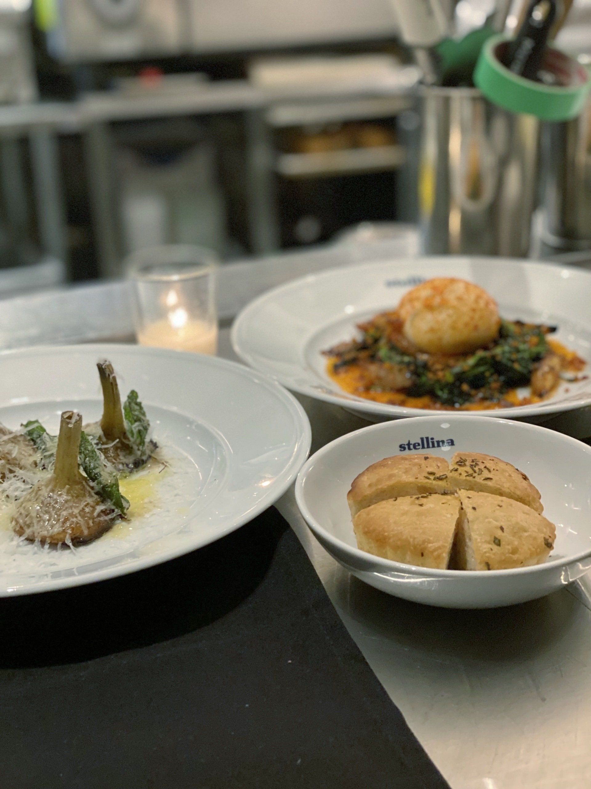 Three plates of food are on a table with a candle in the background