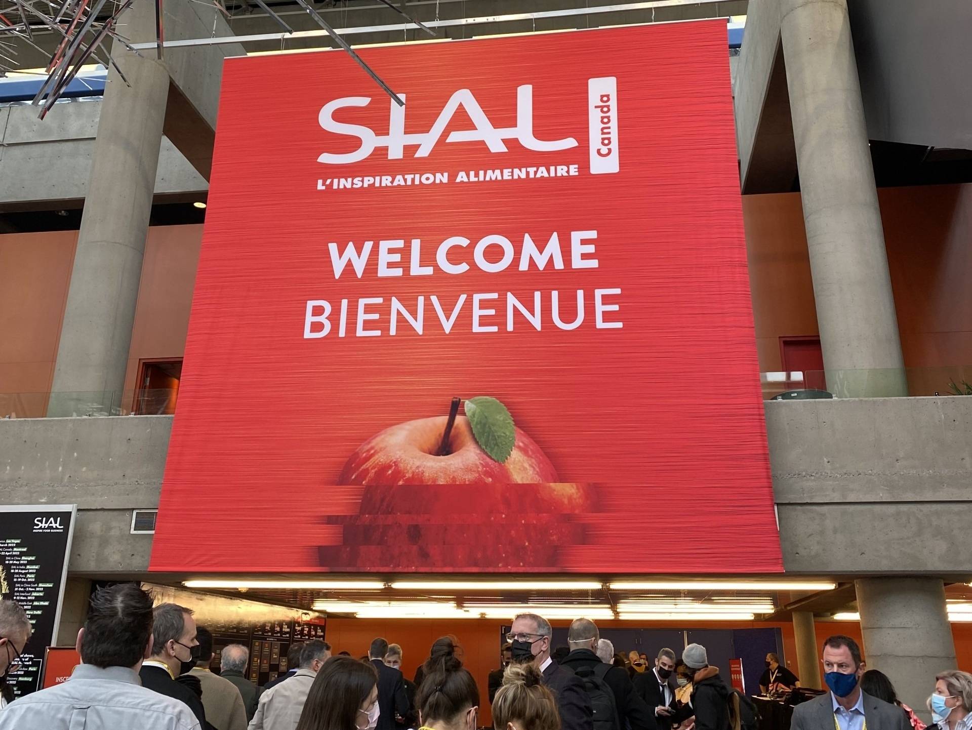 A group of people are standing in front of a large red sign that says welcome bienvenue.