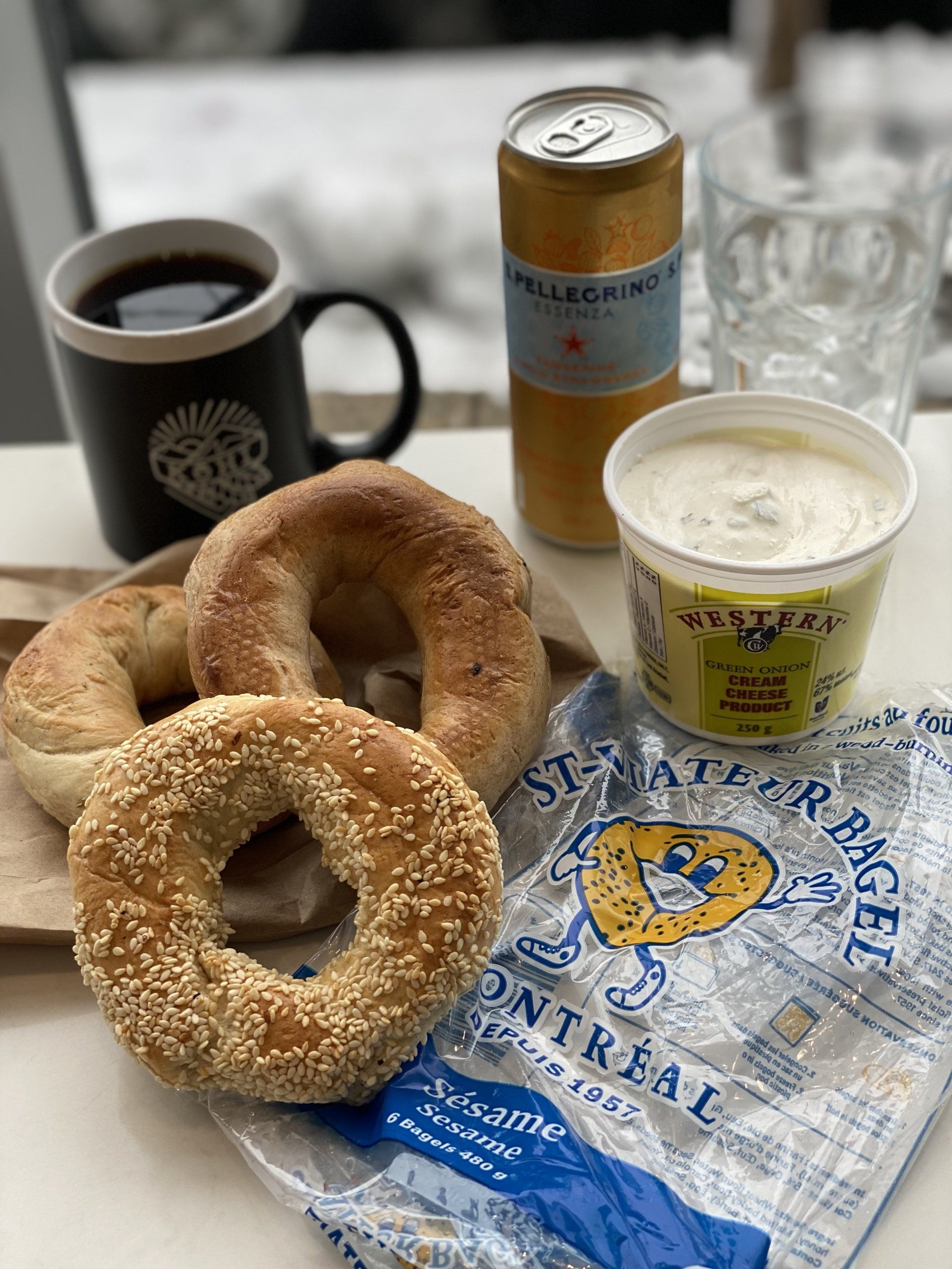 A table topped with bagels , a cup of coffee , a can of soda , and a cup of yogurt.
