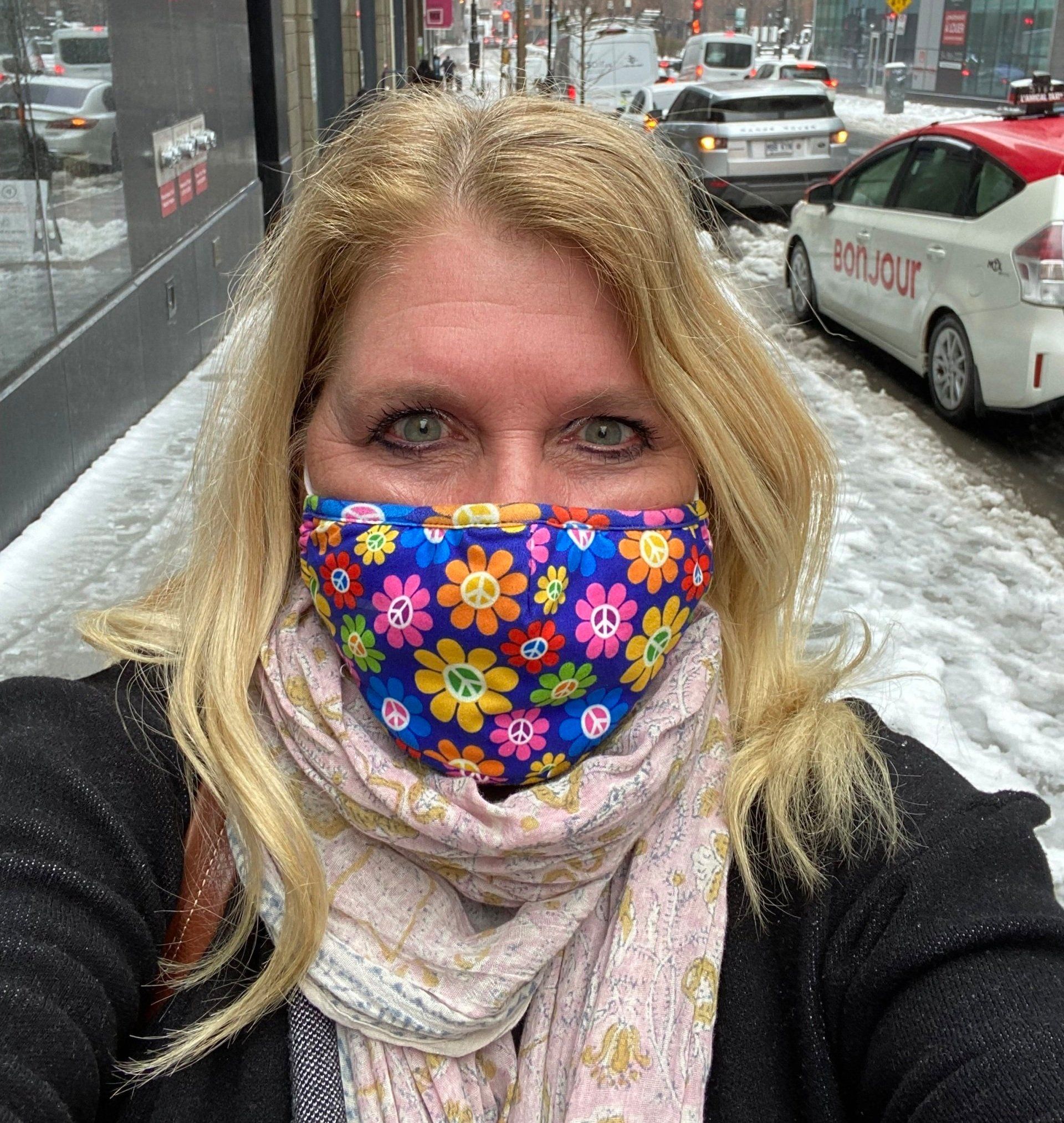 A woman wearing a colorful face mask is taking a selfie on a snowy street.