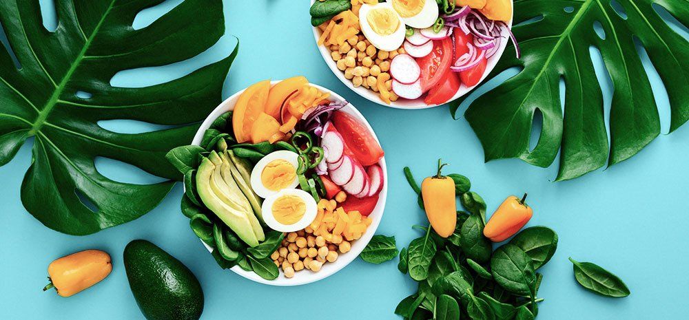 Two bowls of healthy food on a blue table with tropical leaves.