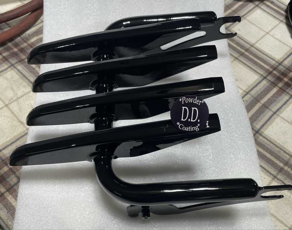 A black motorcycle luggage rack rests on white foam padding, featuring a multi-slat design and mounting brackets.