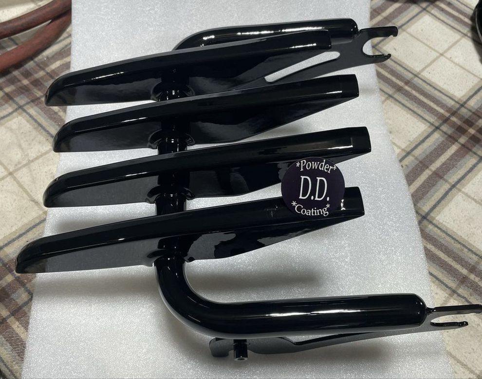 A black motorcycle luggage rack resting on white foam padding, featuring four horizontal bars and mounting brackets.
