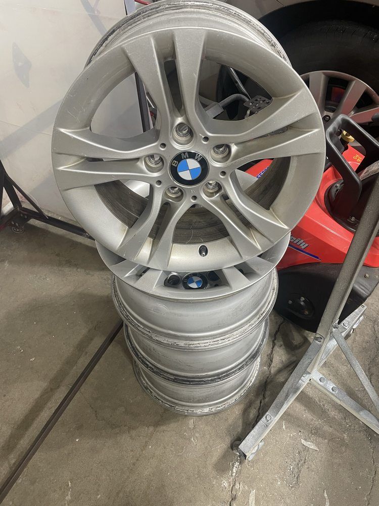 A stack of four silver BMW alloy wheels standing on a garage floor next to a red snowblower.
