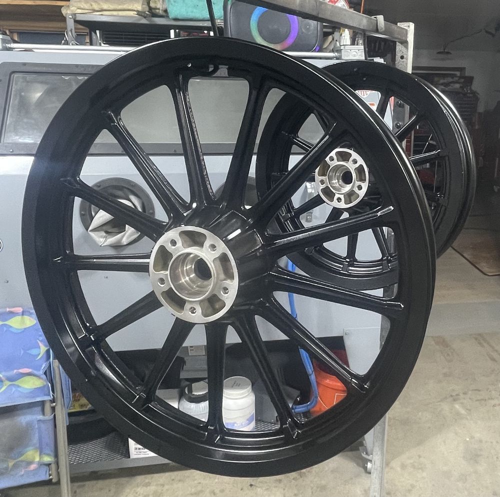 Two glossy black motorcycle wheels with metallic silver hubs mounted on a rack in a garage setting.