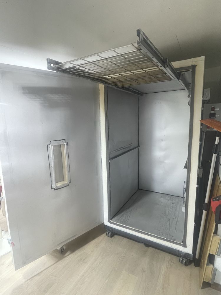 An open, tall, metal cabinet with a wire shelf near the top and a small rectangular window on the door.