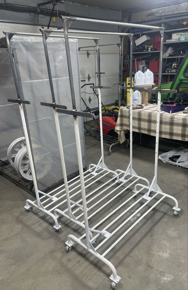 Two empty, white metal double-tier clothing racks on casters stand in a cluttered garage.