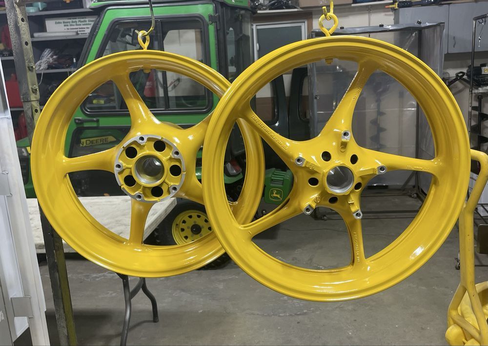Two bright yellow five-spoke motorcycle wheels hang from hooks in a garage or workshop setting.
