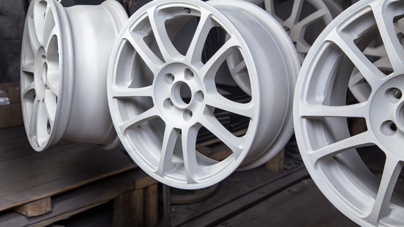 Several white car wheels hanging in a workshop, likely undergoing a powder coating or painting process.
