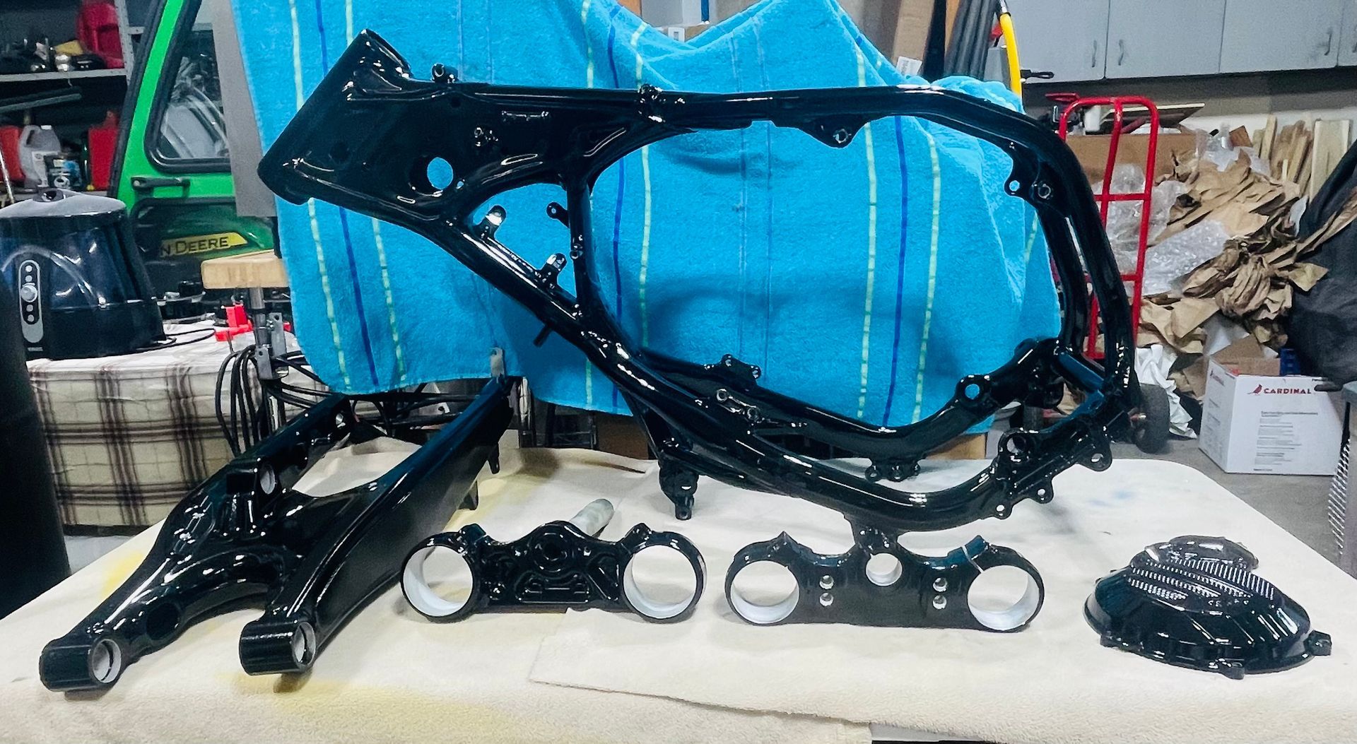 Freshly powder-coated black motorcycle frame, swingarm, triple trees, and engine cover displayed on a workbench.
