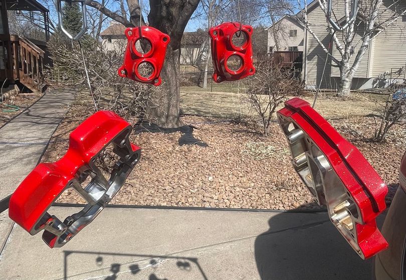 Four bright red automotive brake calipers hanging from wires outdoors to dry after being painted.