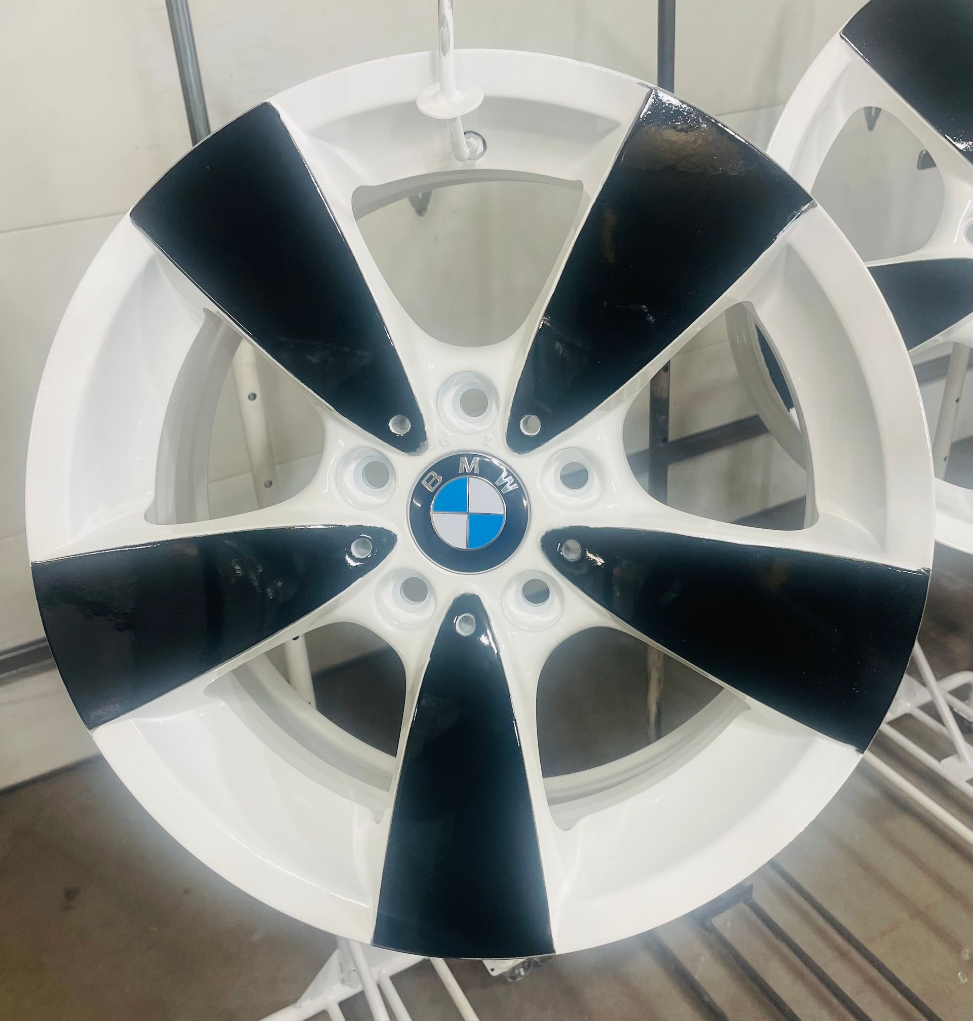 A white and black five-spoke BMW alloy wheel mounted on a stand in a workshop.
