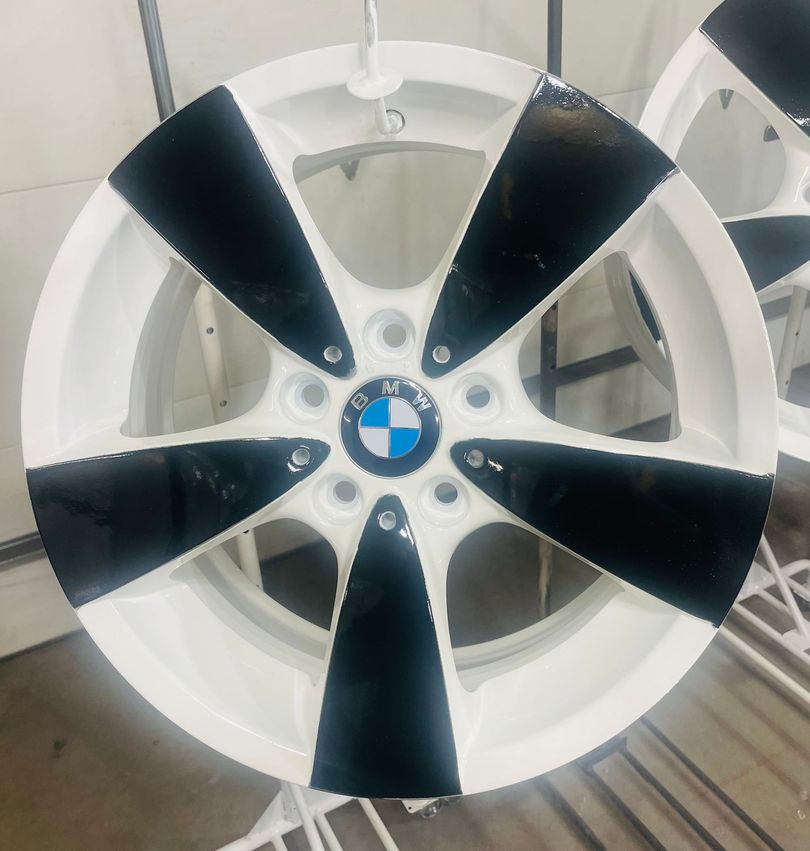 A glossy white and black BMW five-spoke alloy wheel mounted on a workshop stand.