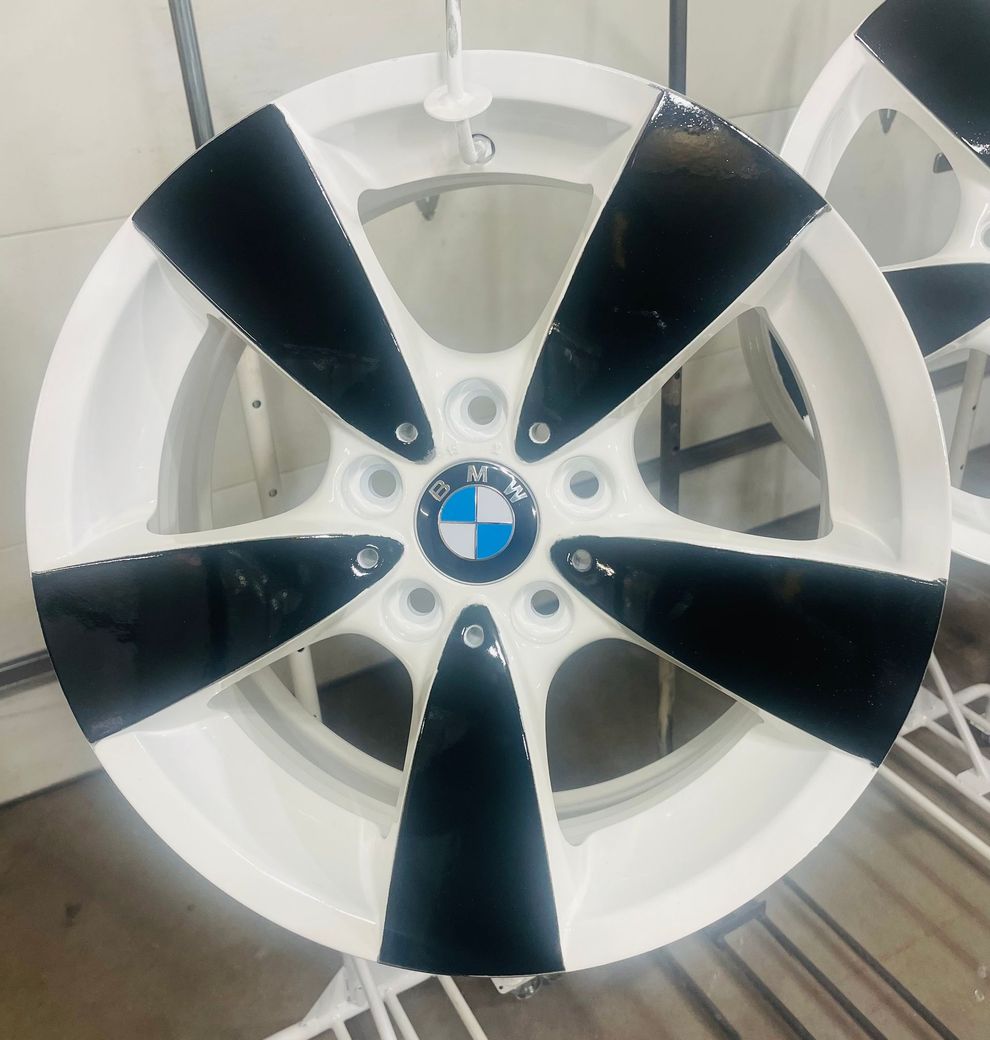 A BMW alloy wheel with a white finish and bold black painted spokes hanging on a rack in a workshop.