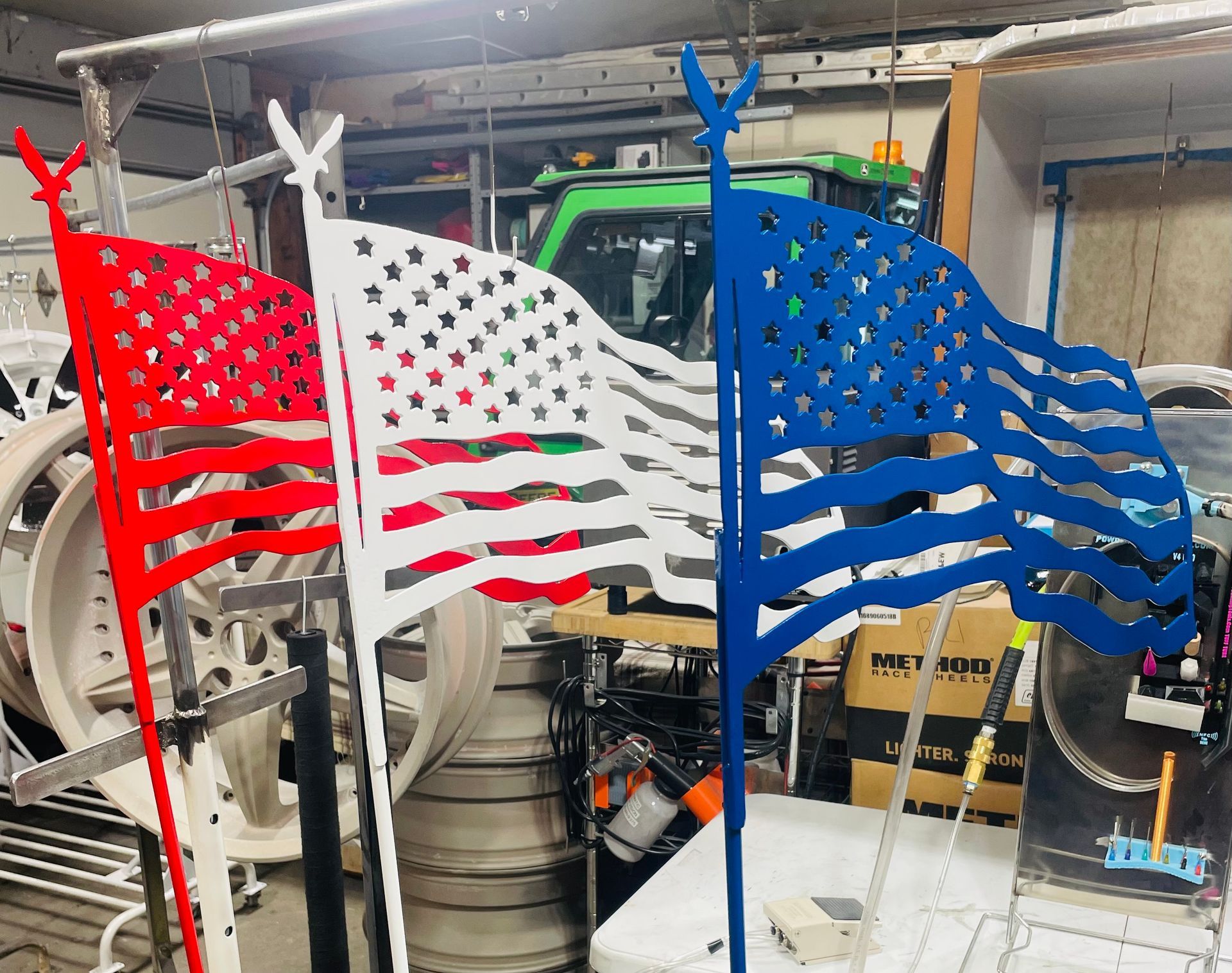 Three metal cutout American flag ornaments, one red, one white, and one blue, each topped with a small eagle silhouette.