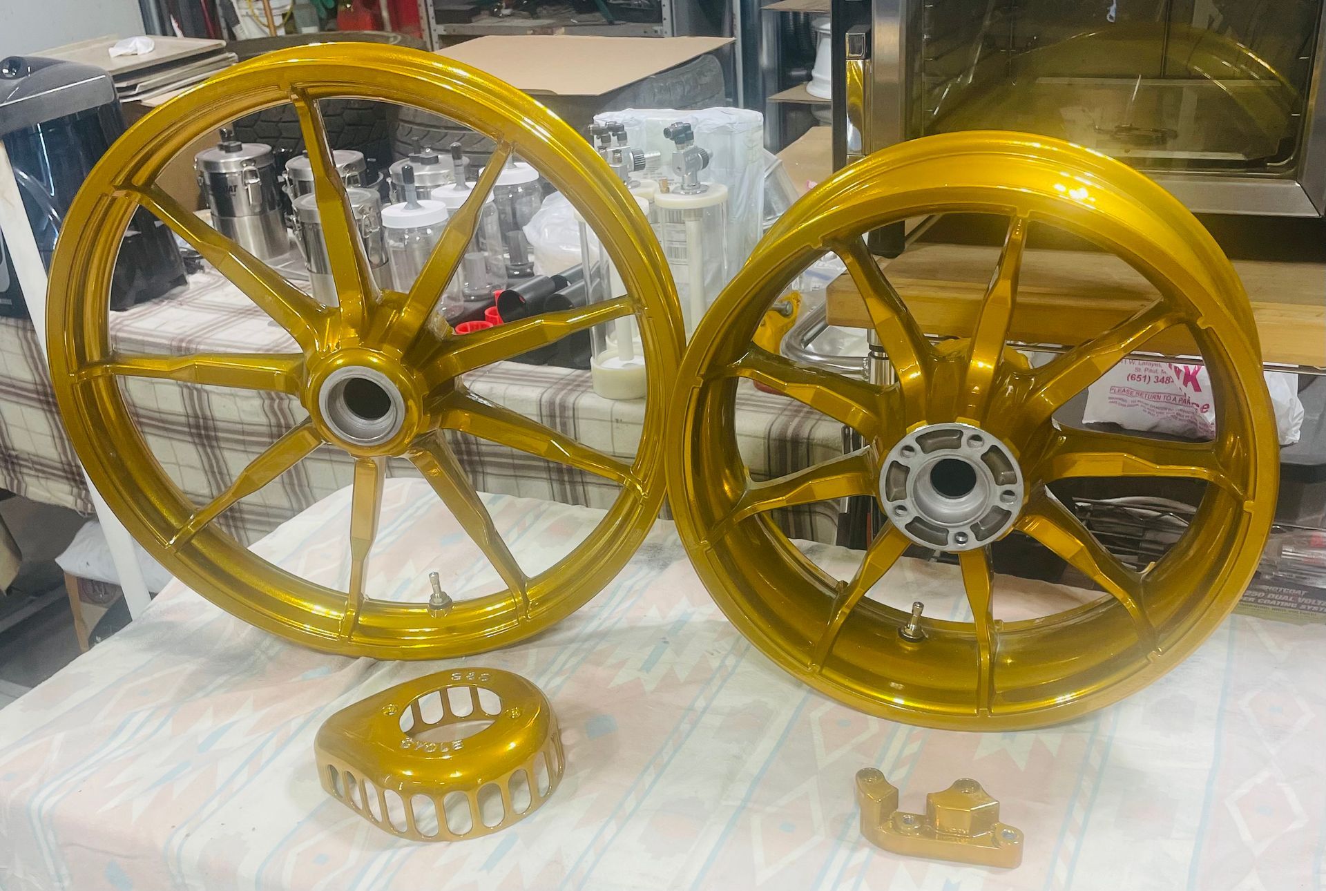 Two gold-painted motorcycle wheels sitting on a table with two matching smaller gold parts.