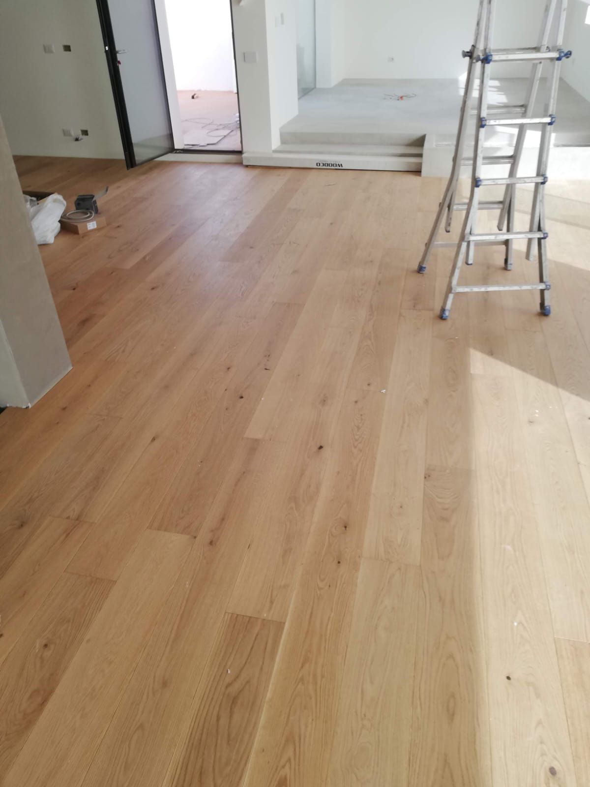 Pavimento in piastrelle di legno chiaro. Il centro presenta un motivo a spina di pesce, incorniciato da un bordo.