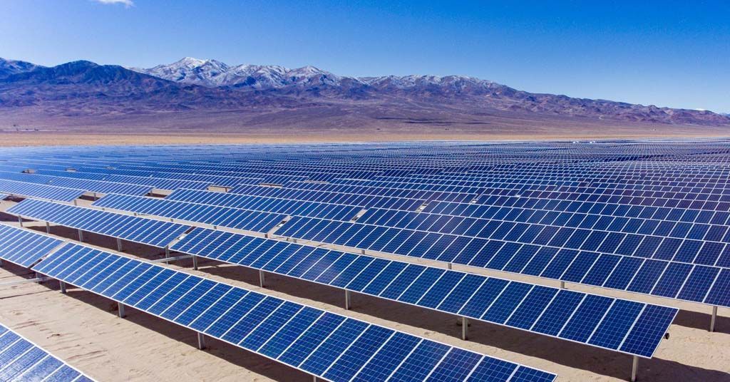 Rows of blue solar panels in a desert with mountains in the distance