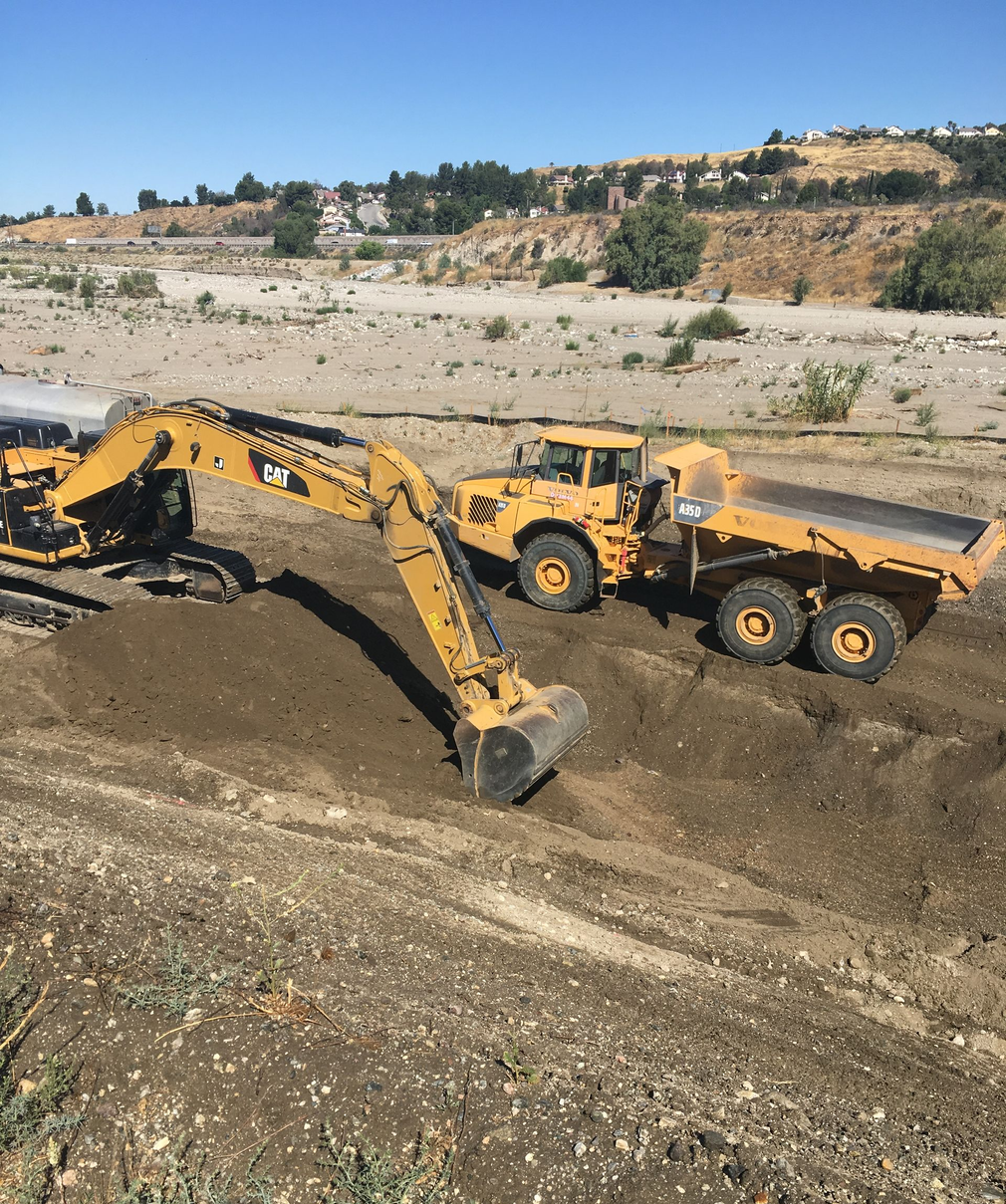 Yellow excavator and dump truck moving dirt at a quarry under a clear blue sky