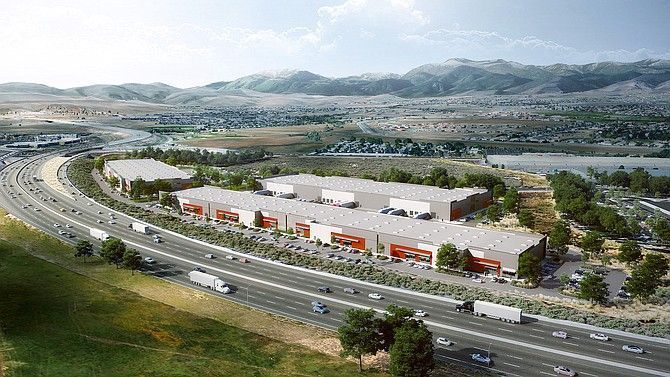Aerial view of a highway beside a large white industrial building with red accents and mountains in the distance