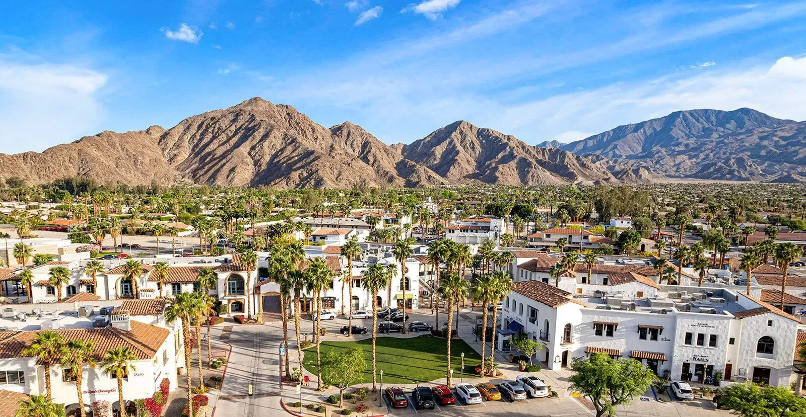 Desert town with white homes and palm trees before rugged mountains under a clear sky