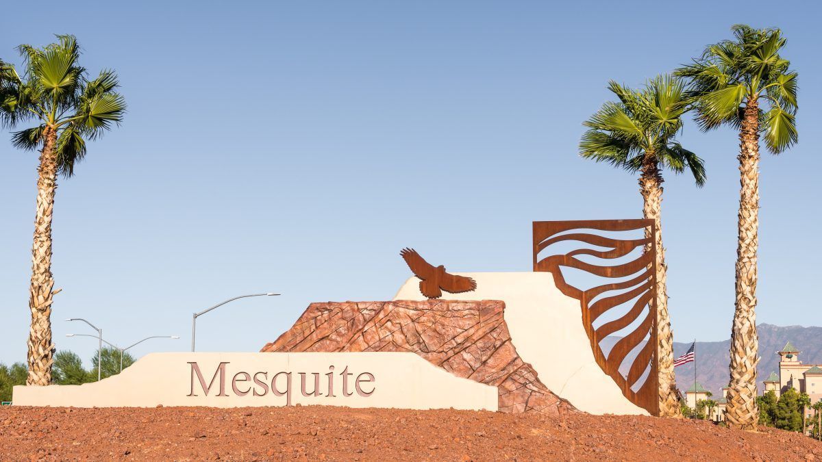 Mesquite entrance sign with desert landscaping, palm trees, and a clear blue sky